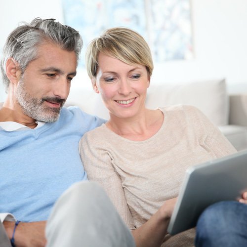 Ein Paaerchen sitzen nebeneinander und schauen auf ein Tablet